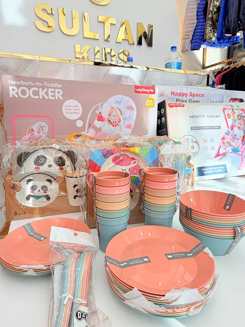 Baby rockers, play gyms and pastel plates, cups and bowls in front of the gold Sultan Kids sign