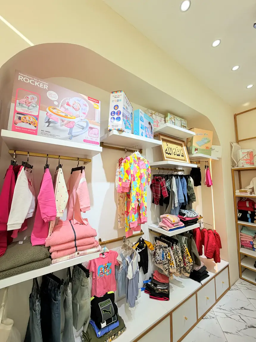The baby wall at Sultan Kids with soft pink outfits, rompers and baby gear on arched shelves