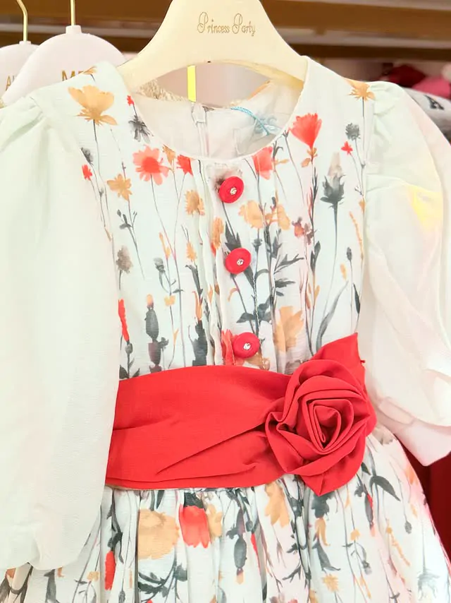 Close up of a flowered party dress with a red satin rose sash
